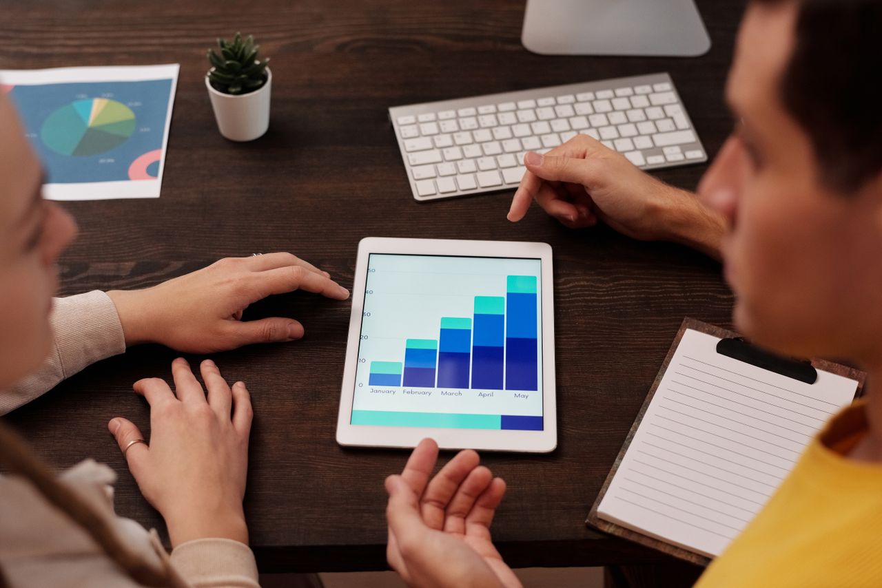 Membres de l’équipe échangeant autour de graphiques numériques sur une tablette, dans un bureau moderne.